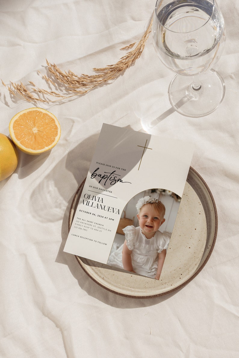 May include: A white baptism invitation with a gold cross and a photo of a baby girl in a white dress. The invitation reads "Please join us for the baptism of our daughter Olivia Villanueva October 06, 2024 at 3PM The All Saint Church 123 Anywhere St. Seattle WA Kindly RSVP to Ana at 123-456-7891 Lunch reception to follow"