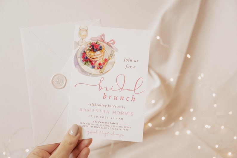 Peut inclure: Une invitation &agrave; un brunch de mariage rose et blanc avec une illustration aquarelle d'une assiette de cr&ecirc;pes avec des baies et un verre de champagne. Le texte indique "rejoignez-nous pour un brunch de mariage c&eacute;l&eacute;brant la future mari&eacute;e Samantha Morris 12.10.2024 &agrave; 16h00 The Pancake Palace 1234 any street, any city, any state, 12345 RSVP &agrave; Michelle au 123-456-7891"