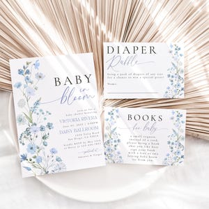 May include: Baby shower invitation with blue floral design. The invitation reads "Baby in Bloom" and includes the details of the event: Victoria Rivera, June 1st, 1:00 PM, Daisy Ballroom. Two additional cards are included, one for a diaper raffle and one for a book request for the baby.