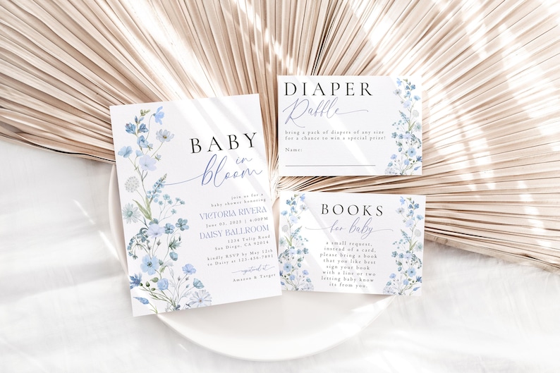 May include: Baby shower invitation with blue floral design. The invitation reads "Baby in Bloom" and includes the details of the event: Victoria Rivera, June 1st, 1:00 PM, Daisy Ballroom. Two additional cards are included, one for a diaper raffle and one for a book request for the baby.