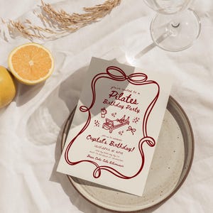 May include: A Pilates birthday party invitation with a red border and text. The invitation includes the text "Pilates Birthday Party" and "Crystal's Birthday!" along with event details. A glass of water and a lemon are also in the image.