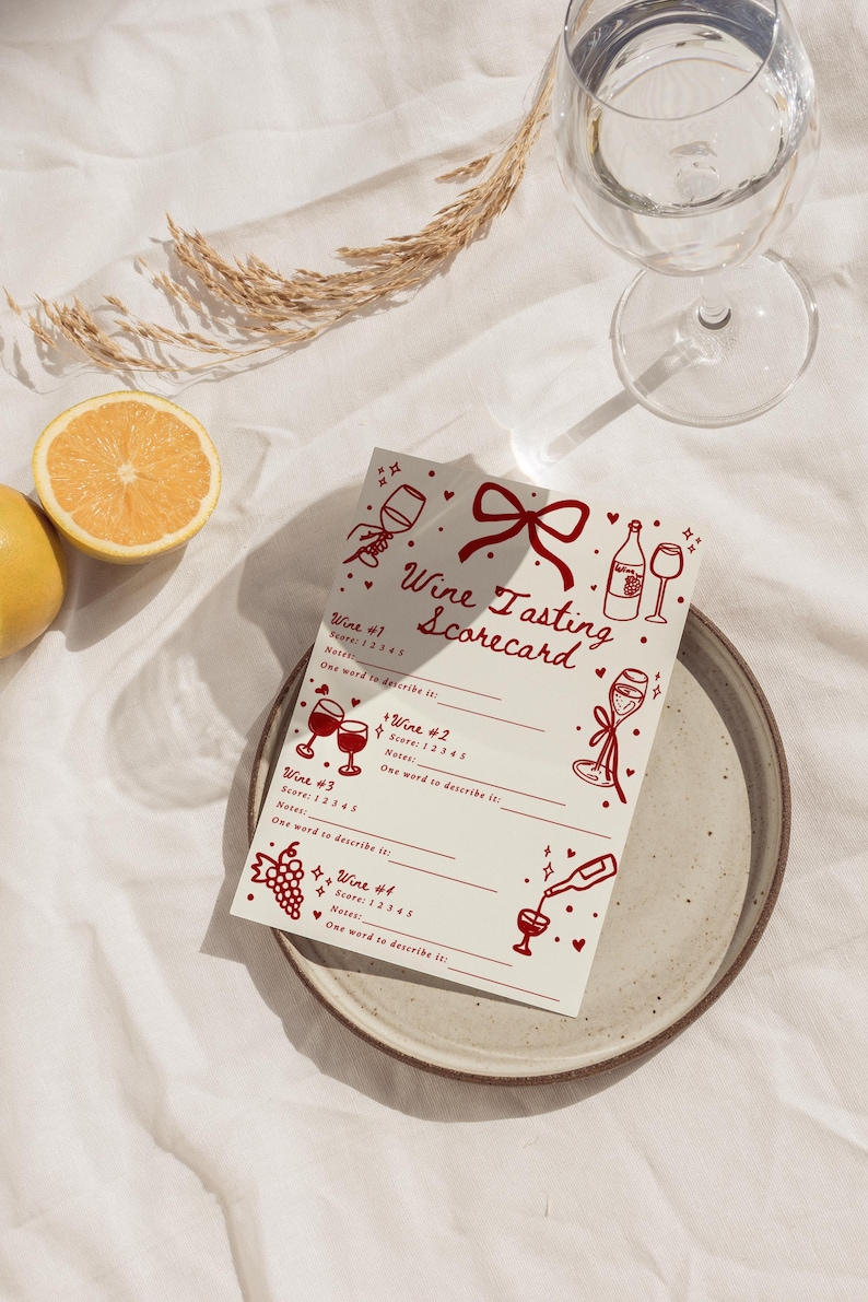 Pu&ograve; includere: Un segnapunti per la degustazione di vini con illustrazioni rosse di bicchieri, bottiglie e un fiocco. Il testo "Wine Tasting Scorecard" &egrave; in alto. La scheda &egrave; su un piatto di ceramica con un limone e un bicchiere d'acqua sullo sfondo.