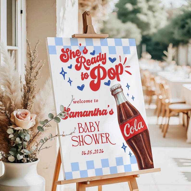 Może przedstawiać: Znak baby shower na sztaludze. Znak ma niebiesko-białe kratkowane tło z czerwonym tekstem, kt&oacute;ry brzmi "She's Ready to Pop" i "Welcome to Samantha's Baby Shower". Prezentowana jest ilustracja butelki coli.
