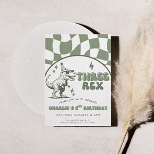 May include: A birthday invitation with a green and white checkered pattern at the top. The invitation features a cartoon dinosaur wearing sunglasses and a party hat, with the text "THREE REX". The invitation is for Charlie's 3rd birthday.