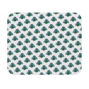 Puede incluir: Una alfombrilla de ratón rectangular blanca con un patrón repetido de insectos estilizados azules y verdes. Los insectos tienen alas azules y cuerpos verdes, dispuestos en forma de cuadrícula sobre la superficie.