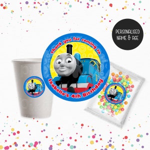 May include: An image with Thomas the Tank Engine party decorations. Includes a white cup, a bag of sweets, and circular stickers with the text "Thank you for coming to Isabella's 4th Birthday".