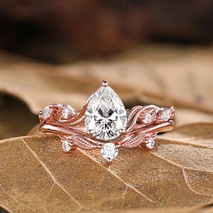 May include: Rose gold engagement ring set with a pear-shaped center stone and delicate leaf accents.