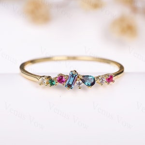 May include: A delicate gold band ring with a cluster of colourful gemstones. The ring features a mix of round, pear-shaped, and rectangular stones in shades of pink, green, and blue.