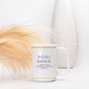 Peut inclure: Une tasse en c&eacute;ramique blanche avec une bande dor&eacute;e et du texte qui dit "Gracias por tu duro trabajo Natalie Traes gran alegria a nuestra familia".