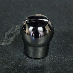 May include: A chrome gear shift knob with a rounded top and a groove around the top edge.