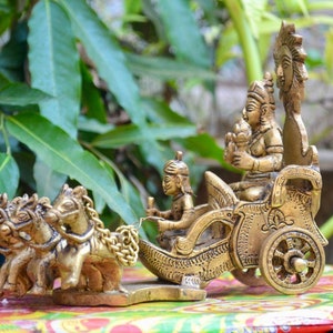 Op de afbeelding: Een gouden metalen sculptuur van een wagen getrokken door drie paarden. De wagen is versierd met ingewikkelde details en heeft een figuur van een godheid die op een troon zit.