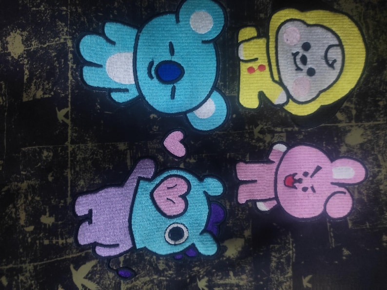 May include: Four colorful cartoon characters with different facial expressions and body shapes. The characters are embroidered on a dark fabric background.