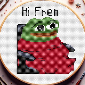May include: Cross-stitch embroidery hoop featuring a green frog meme wearing a red shirt, sitting in a chair. The text "Hi Fren" is above the frog.