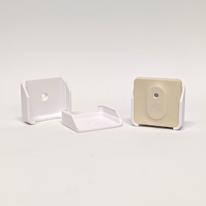 Op de afbeelding: Drie witte kunststof wandbevestigingen, twee zijn vierkant en één is rechthoekig. De rechthoekige bevestiging heeft een beige vierkante sensor met een klein rond gat in het midden.