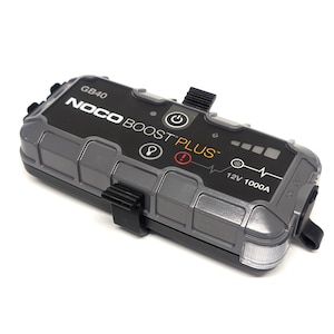 May include: A grey NOCO BOOST PLUS GB40 portable jump starter with a black strap and a white LED light. The device has a digital display showing 12V 1000A.