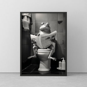 Könnte beinhalten: Schwarz-Weiß-Druck in einem Rahmen, der einen Frosch zeigt, der auf einer Toilette sitzt und eine Zeitung liest. Der Frosch ist der Mittelpunkt, mit der Toilette und dem Badezimmer als Hintergrund. Eine humorvolle Darstellung.