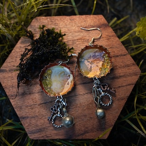 May include: A pair of earrings made from bottle caps with a gold and white resin design. Each earring has a silver charm with a key, a heart, and a pearl.