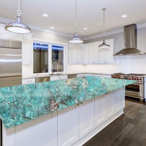 May include: A modern kitchen with white cabinets, stainless steel appliances, and a large island with a turquoise countertop. The kitchen features pendant lights, a range, and a stainless steel refrigerator.