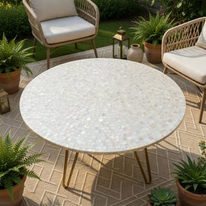 May include: A round outdoor coffee table with a mosaic tile top in shades of white and cream. The table has gold-colored hairpin legs. The table is surrounded by outdoor furniture and potted plants.