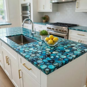 May include: A kitchen island with a striking blue agate countertop. The countertop is made of circular, polished stones in shades of blue and white. A stainless steel sink and faucet are installed. White cabinets with gold hardware complete the look.