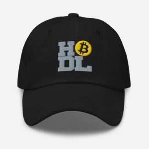 May include: A black baseball cap featuring embroidered text that reads HODL in a blocky, light grey font. The letter O is replaced by a circular, yellow embroidered Bitcoin symbol. The cap has a structured crown and a curved brim.
