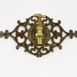 Puede incluir: Grifo de estilo antiguo en latón montado sobre una placa trasera decorativa de hierro fundido. La placa trasera tiene un acabado envejecido y presenta intrincados diseños de volutas y florales. El diseño del grifo evoca encanto vintage.