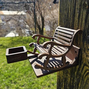 May include: A wooden bird feeder shaped like a rocking chair with a small square wooden tray attached to the side. The feeder is mounted on a wooden post.