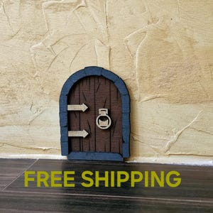 May include: A small wooden door with a brown finish and a black frame. The door has a rounded archway and a metal ring door knocker. The door is mounted on a beige wall with the text "FREE SHIPPING" printed on the floor below.