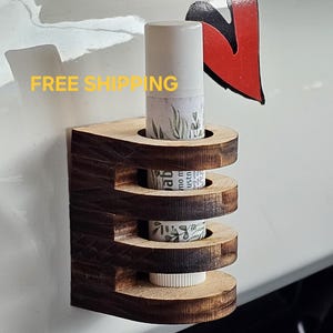 May include: A wooden lip balm holder with three slots, designed to hold lip balm tubes. The holder is attached to a white surface with a magnetic backing. The holder is made of dark wood with a natural wood finish. The lip balm holder is a great way to keep your lip balm organized and accessible.