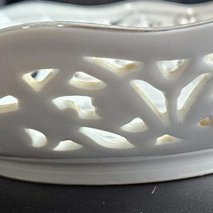 May include: White ceramic bowl with a scalloped rim and intricate cut-out design. The bowl has a delicate, lacy appearance.