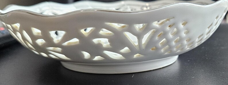 May include: White ceramic bowl with a scalloped rim and intricate cut-out design. The bowl has a delicate, lacy appearance.