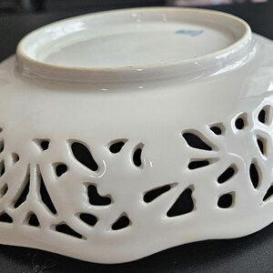 May include: White porcelain bowl with a scalloped edge and intricate cut-out design. The bowl has a delicate floral pattern.