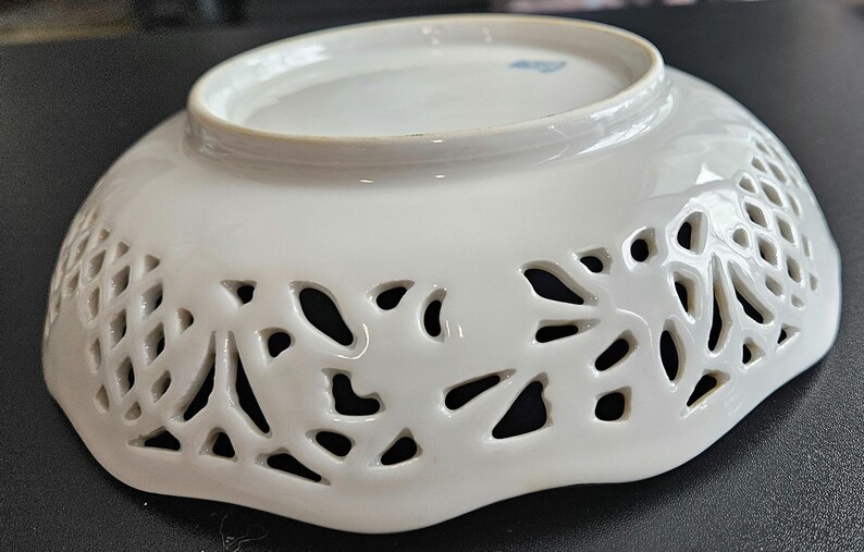 May include: White porcelain bowl with a scalloped edge and intricate cut-out design. The bowl has a delicate floral pattern.
