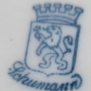 May include: A blue and white porcelain mark with a crowned lion and the text "Schumann" underneath.