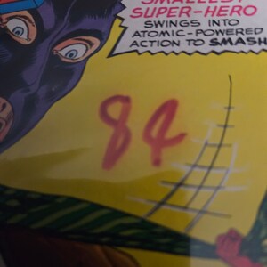 K&ouml;nnte beinhalten: Ein Comic-Cover mit einem maskierten Superhelden in einem rot-blau-gelben Kost&uuml;m. Der Text auf dem Cover lautet "THE BIGGER THEY ARE, THE HARDER THEY FALL - WHEN THE WORLD'S SMALLEST SUPER-HERO SWINGS INTO ATOMIC-POWERED ACTION TO SMASH". Die Zahl 84 ist in Rot auf gelbem Hintergrund geschrieben.