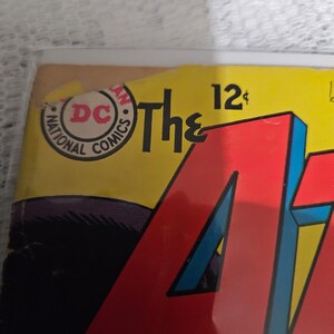 K&ouml;nnte beinhalten: Ein Vintage-Comic-Cover mit einem roten, blauen und gelben "A" mit dem Text "The" und "12&cent;" dar&uuml;ber. Das Cover zeigt auch einen runden Aufkleber mit dem Text "National Comics" und "DC" in einem roten Kreis.