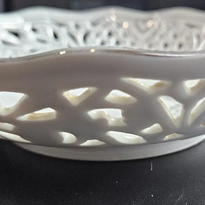 May include: White ceramic bowl with a delicate, intricate cut-out design. The bowl has a scalloped edge and a smooth, glossy finish.
