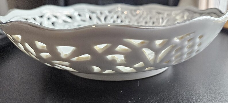 May include: White ceramic bowl with a delicate, intricate cut-out design. The bowl has a scalloped edge and a smooth, glossy finish.