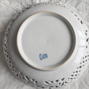 May include: White ceramic bowl with a delicate, openwork design. The bowl has a round shape and a smooth, white glaze. The bottom of the bowl features a blue and white logo with the text "Germany" in blue.