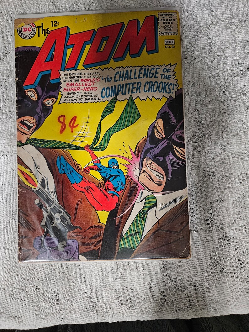 K&ouml;nnte beinhalten: Ein Comic-Cover mit einem Superhelden namens The Atom. Das Cover ist gelb mit gr&uuml;nen und roten Akzenten. The Atom k&auml;mpft gegen einen Schurken, der eine violette Maske tr&auml;gt. Der Text auf dem Cover lautet "The Challenge of the Computer Crooks!"