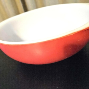 May include: A red and white mixing bowl with a white interior and a red exterior. The bowl is made of ceramic and has a rounded shape.