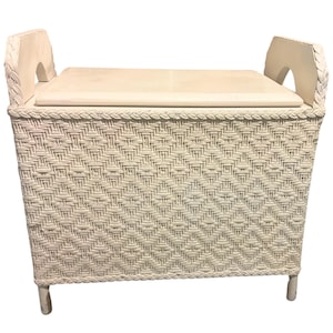 Puede incluir: Banco de almacenamiento tejido de color blanquecino con un asiento rectangular y dos asas curvas. El banco presenta un tejido con patrón de diamantes y está sostenido por cuatro patas cortas. Las asas tienen un diseño trenzado.