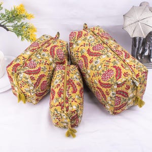 Puede incluir: Tres bolsas de cremallera de tela amarilla con un patrón floral rojo y blanco. Las bolsas son de diferentes tamaños y tienen borlas.