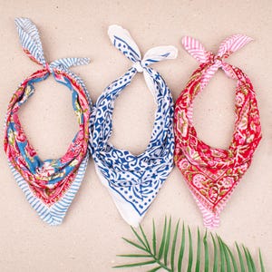 May include: Three patterned bandanas in a row. One is blue and red with a floral design, another is white with blue patterns, and the third is red and pink with a floral design. Each is knotted at the top.