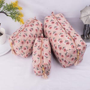May include: Three quilted fabric zippered pouches in various sizes with a floral print in shades of pink, green, and white. The pouches have gold zipper pulls and tassels.