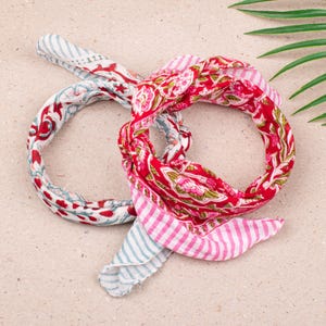 Può includere: Due bandane colorate annodate insieme. Una è rossa con un motivo floreale, l'altra bianca con disegni floreali rossi e blu. Le bandane presentano colori vivaci e motivi vari, perfette per aggiungere un tocco di stile.