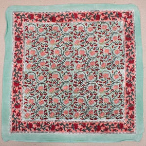 May include: A square, floral-patterned textile with a light green border. The interior features a repeating pattern of pink flowers and green leaves on a light blue background. A pink border with red floral accents frames the central design.
