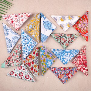 Pode incluir: Uma coleção de guardanapos de tecido coloridos e estampados dispostos sobre uma superfície clara. Os guardanapos apresentam vários desenhos, incluindo motivos florais, geométricos e de peixes, em tons de vermelho, azul, amarelo e verde. Os guardanapos são dobrados em triângulos.