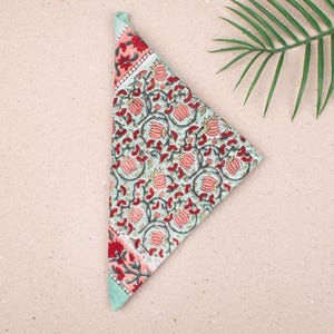May include: A folded, triangular cloth napkin with a floral pattern. The napkin features a light blue background with red and pink floral designs and a red and pink border. The napkin is made of a soft fabric.