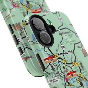 May include: A green and white phone case with a map of Franconia, New Hampshire. The case features a map with roads, towns, and landmarks, including Cannon Mountain, Franconia Notch State Park, and the Profile Lake. The case also features a black camera lens cutout.